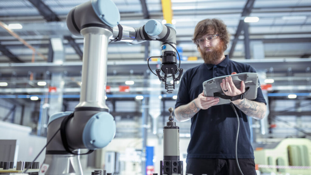 Image of a man with a computer tablet standing in front of an industrial robotic arm.
