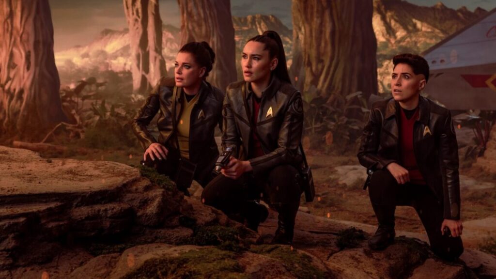 Enterprise crew members on an alien planet hunched down and surveying the terrain