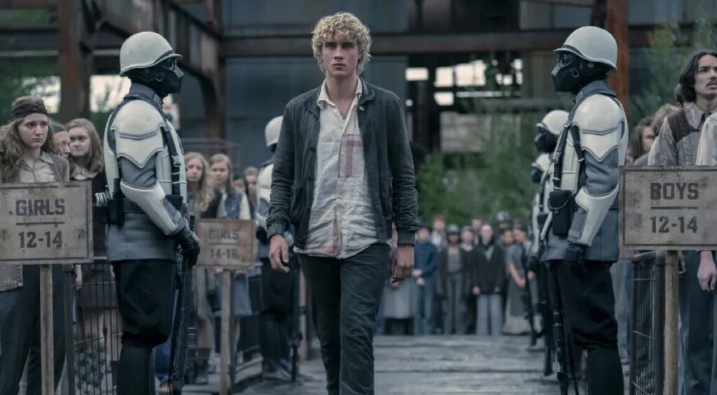 young man with tousled blonde hair walking between two rows of potential tributes
