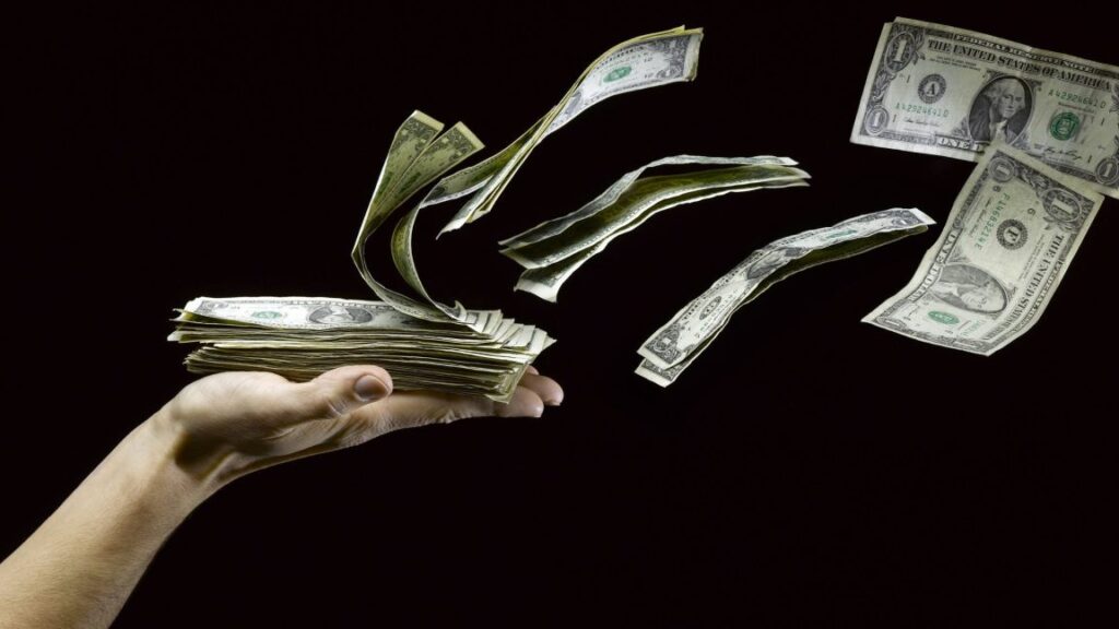 A stack of $1 bills getting blown off a person's hand.