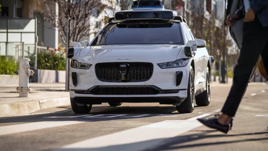 A white Waymo Jaguar I-Pace drives on a road.